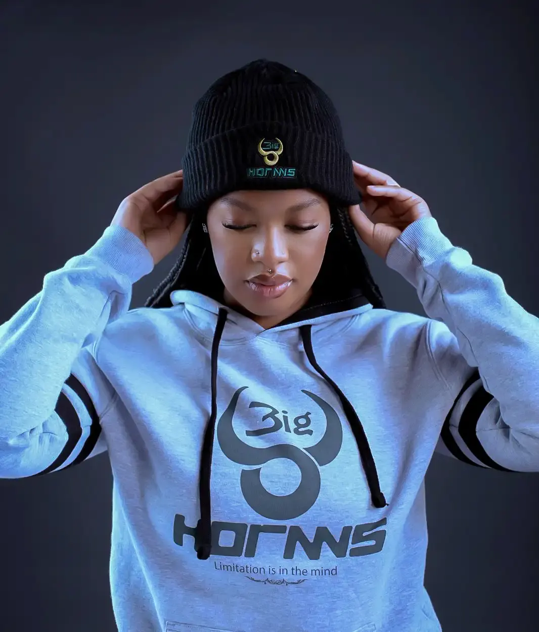Woman pulling on a black Bighornns beanie, wearing a grey crest hoodie